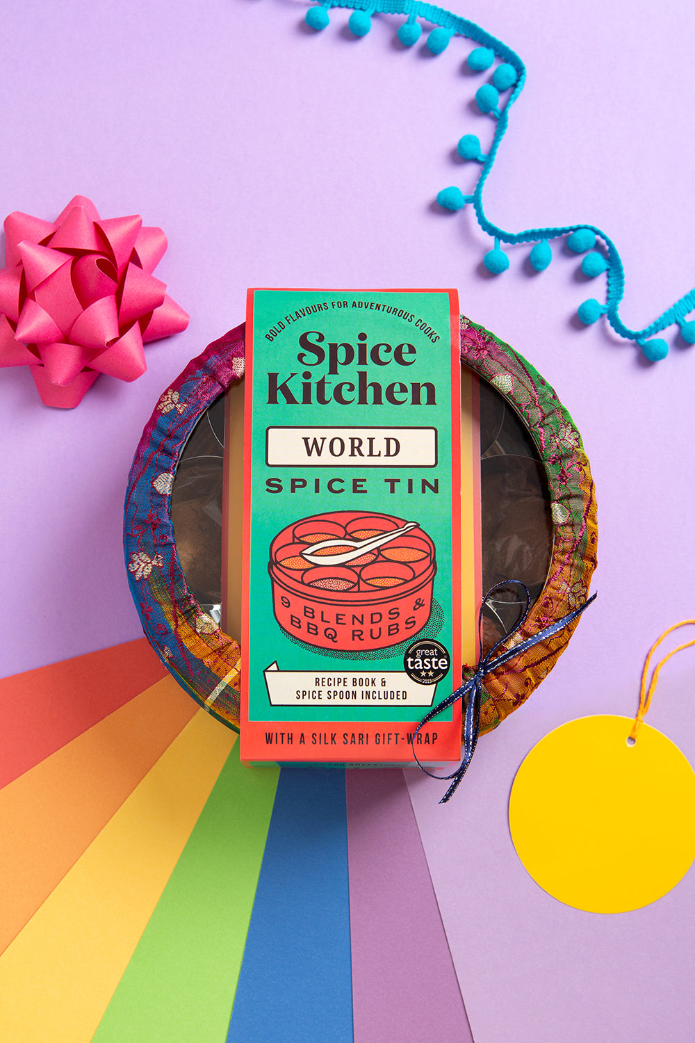 Spice Kitchen Pride Tin World Spice Tin on a colourful background with a pink bow and blue tassels.