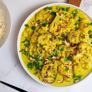 A turmeric-infused cauliflower and coconut curry sprinkled with toasted cashew nuts and fresh coriander, served with a bowl of white rice