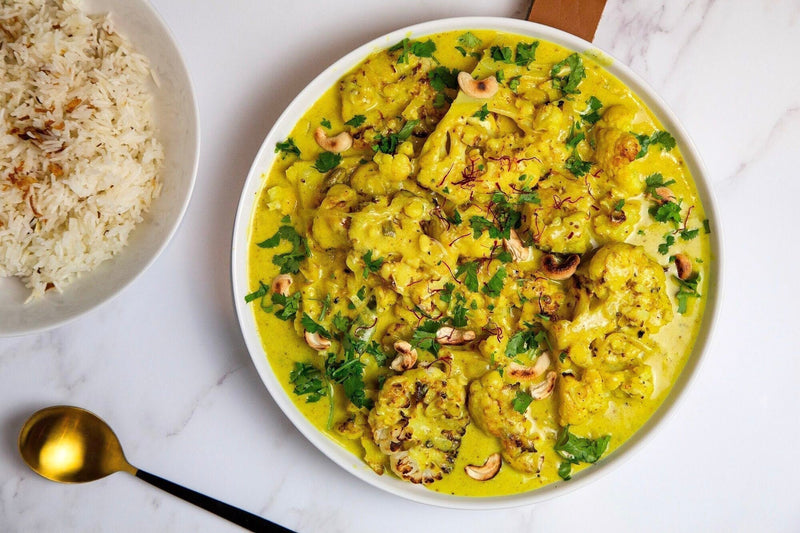 A turmeric-infused cauliflower and coconut curry sprinkled with toasted cashew nuts and fresh coriander, served with a bowl of white rice