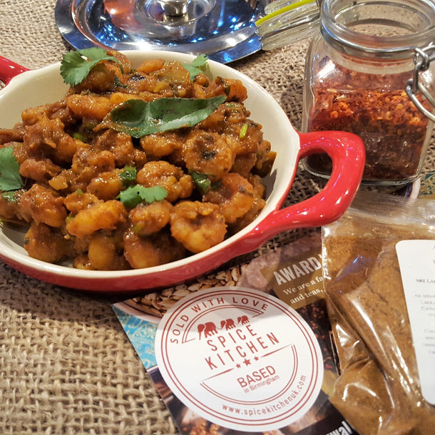 Dry prawn masala curry served in a tomato red ceramic pan with scattered fresh coriander