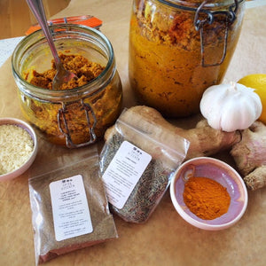 A jar of masala curry paste surrounded by ingedients including garlic, ginger, lemon and Spice Kitchen's garam masala blend