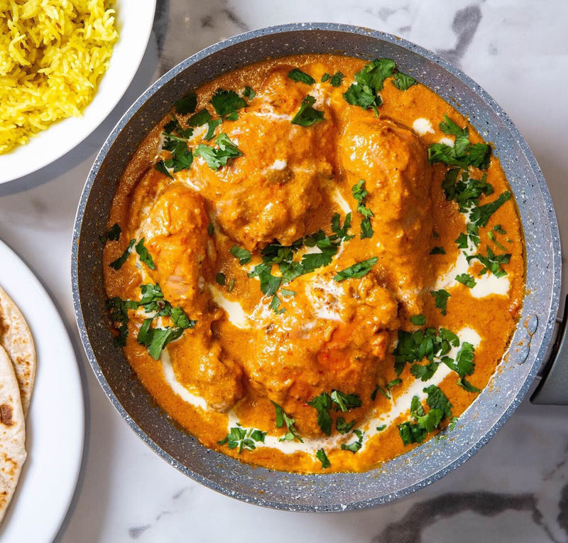 Rich Butter Chicken, garnished with fresh coriander and cream and served with pilau rice and parathas