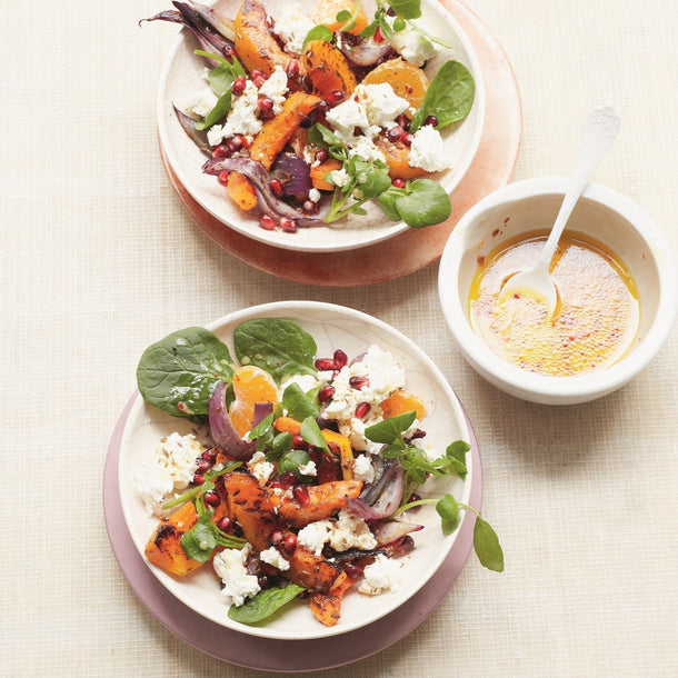 Fresh bowls of winter salad with pumpkin, goat's cheese, spinach and pomegranate seeds, served with a bowl of dressing