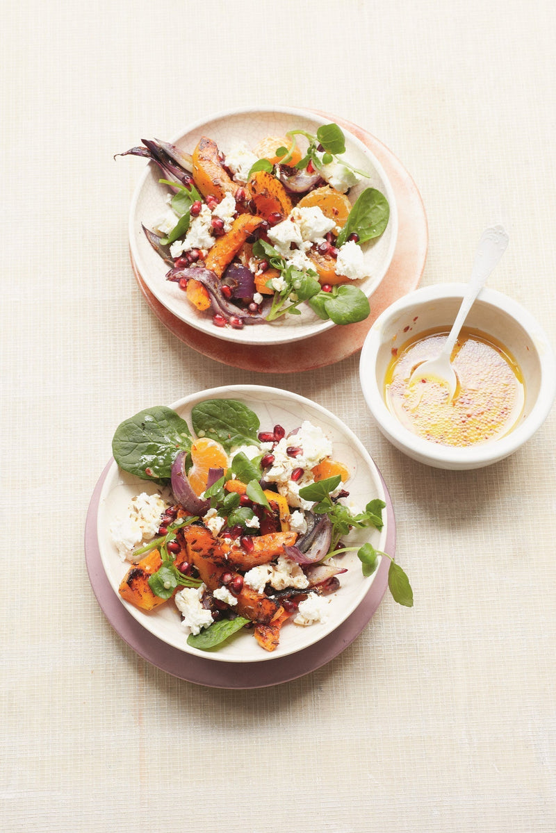 Fresh bowls of winter salad with pumpkin, goat's cheese, spinach and pomegranate seeds, served with a bowl of dressing