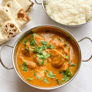 Photograph of chicken tikka masala with white rice and naan bread on a white background