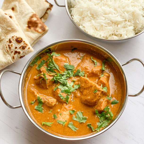 Photograph of chicken tikka masala with white rice and naan bread on a white background