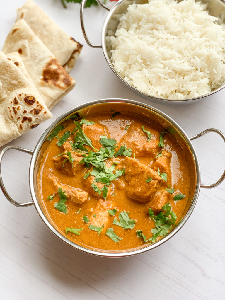 Photograph of chicken tikka masala with white rice and naan bread on a white background