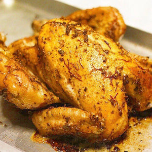 A golden whole roasted chicken basted in buttery saffron on a baking tray
