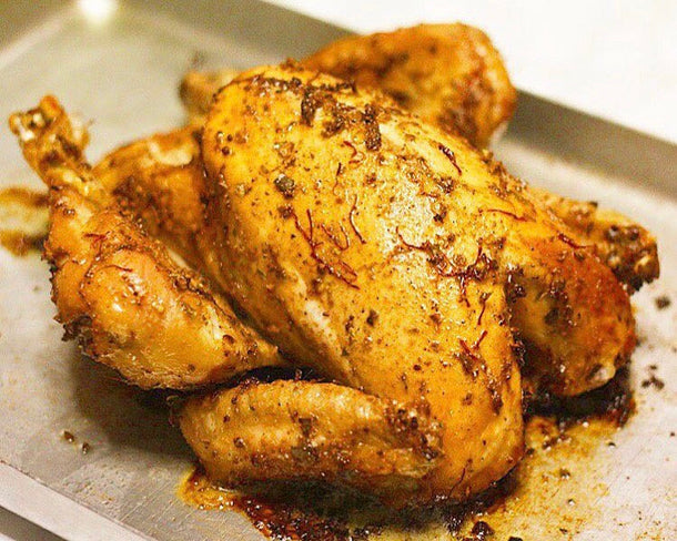 A golden whole roasted chicken basted in buttery saffron on a baking tray
