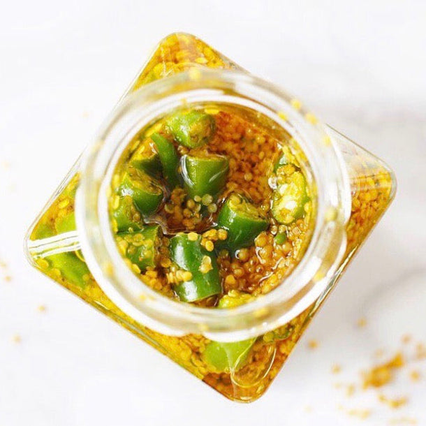 A view inside a jar of colourful fresh chilli, turmeric and lime pickle with generous chunks of green chillies