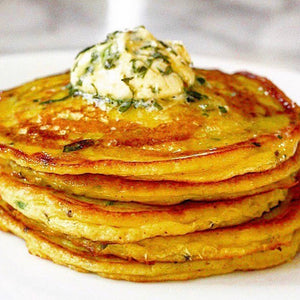 A stack of golden, crispy, spiced potato pancakes garnished with a fresh coriander, lime and chilli butter