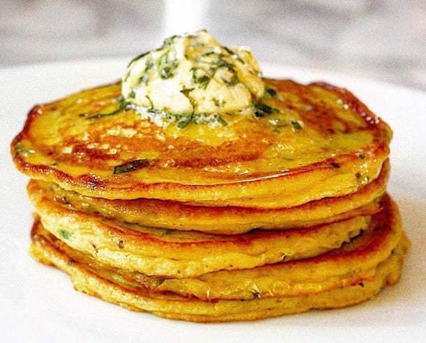 A stack of golden, crispy, spiced potato pancakes garnished with a fresh coriander, lime and chilli butter