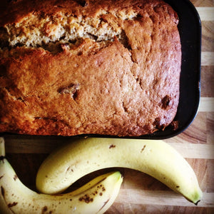 Homemade banana bread loaf with ripe bananas on wooden board