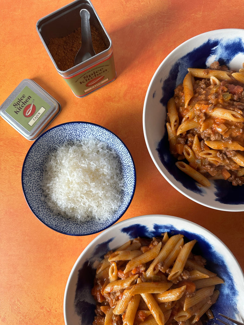 Two bowls of Cajun Ragu Placed next to a small bowl of Parmesan and a Spice Kitchen spice tin.  
