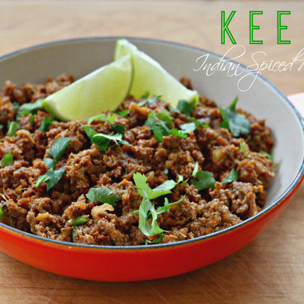 Keema (Indian Spiced Minced Meat) in a red frying pan, garnished with fresh coriander and wedges of lime