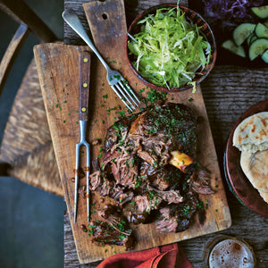 A gorgeous Tender partly shredded lamb joint on a chopping board surrounded by a Pita, Salad and dips. 