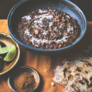 Dal Makhani in a rustic ceramic bowl, with a swirl of fresh cream and wedges of lime and torn naan bread on the side