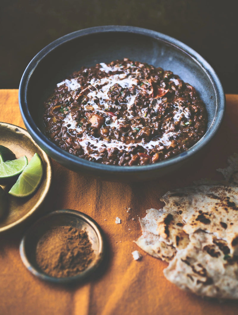 Dal Makhani in a rustic ceramic bowl, with a swirl of fresh cream and wedges of lime and torn naan bread on the side