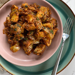 Classic Indian Bombay Potatoes served in a pastel pink bowl on a mint green plate.