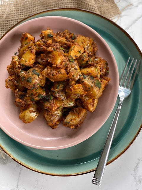 Classic Indian Bombay Potatoes served in a pastel pink bowl on a mint green plate.