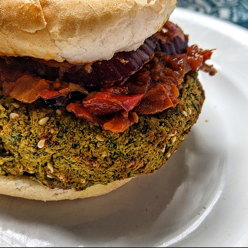 Vegan green falafel burger with a herby falafel patty, fresh salad, and shakshuka chutney in a soft bun.