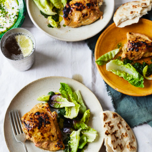 Tandoori chicken featuring marinated chicken pieces roasted until charred, with a smoky red spice coating and herbs.