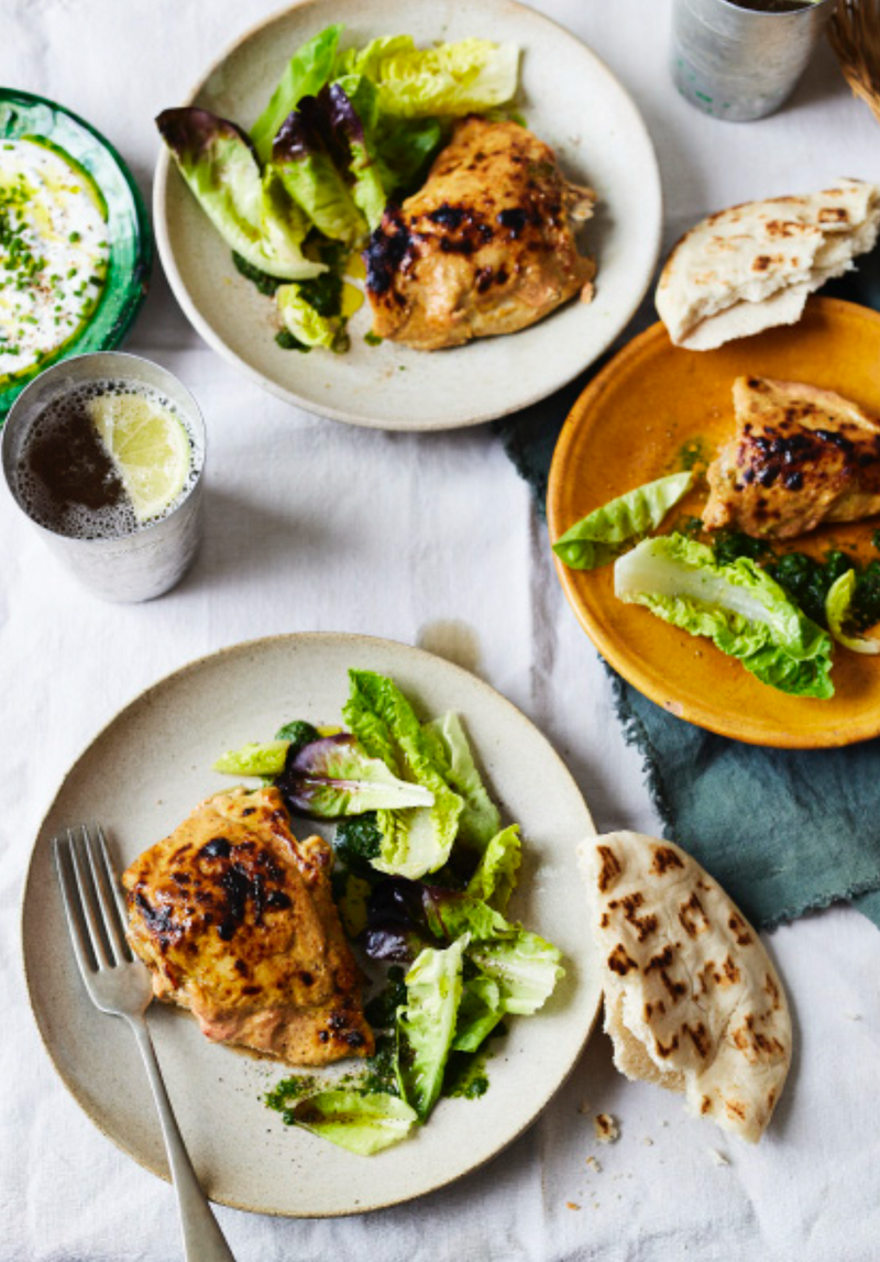 Tandoori chicken featuring marinated chicken pieces roasted until charred, with a smoky red spice coating and herbs.