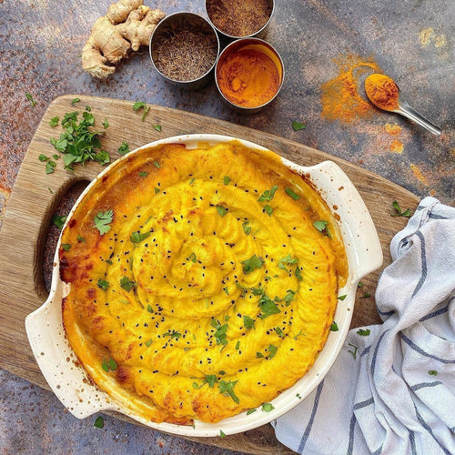A warming shepherd's pie served in a white casserole dish with spice ingredients on the side