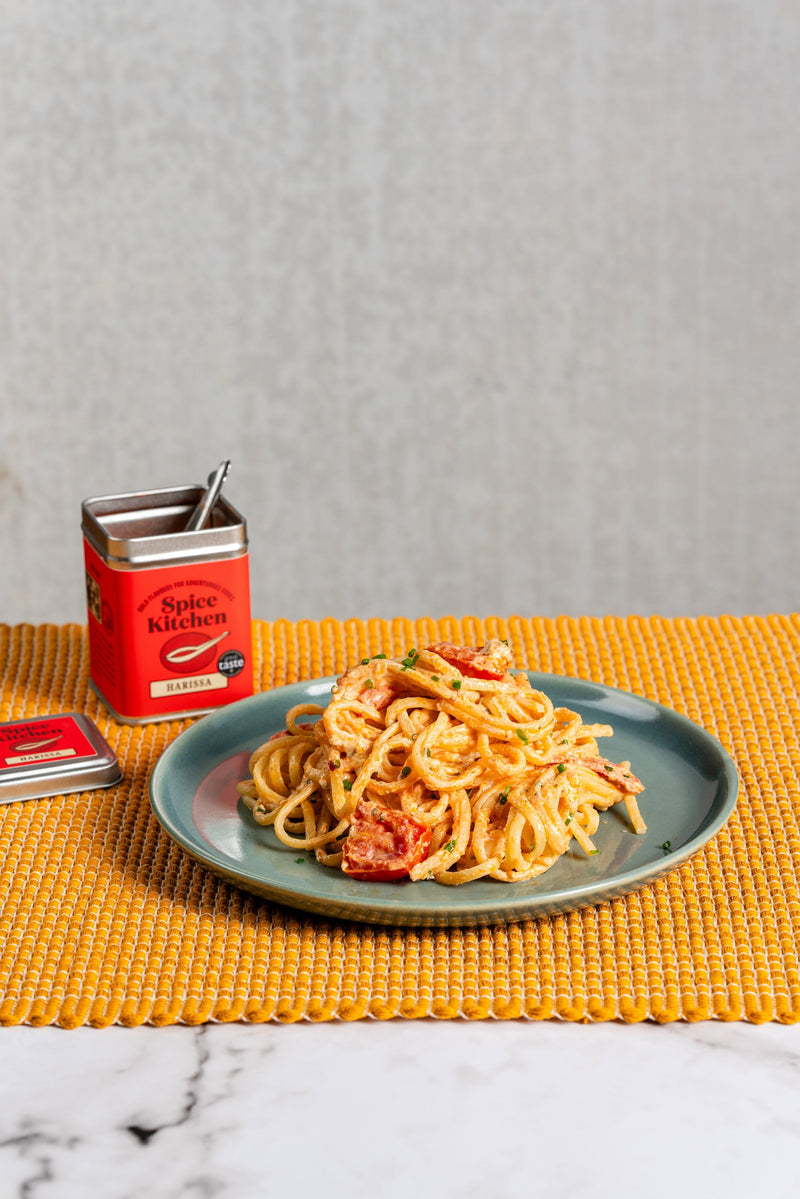 A perfectly cooked portion of Spice Kitchen’s Harissa & Boursin Linguine on a plate next to a Spice Kitchen Harissa tin.