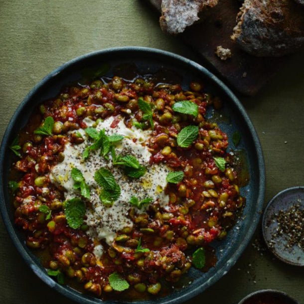 Broad Bean, Tomato & Harissa Stew served in a bowl next to a loaf of bread 