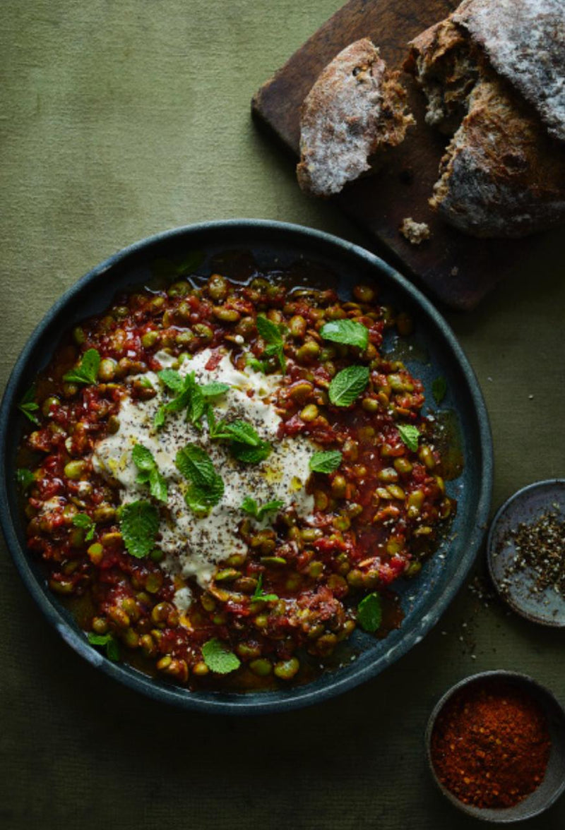 Broad Bean, Tomato & Harissa Stew served in a bowl next to a loaf of bread 