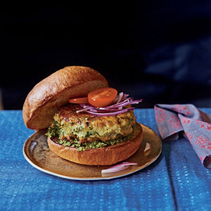 Mumbai-style chicken burger (or pattie) served in a toasted white bun, garnished with slices of red onion and fresh tomato
