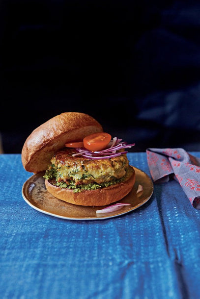 Mumbai-style chicken burger (or pattie) served in a toasted white bun, garnished with slices of red onion and fresh tomato