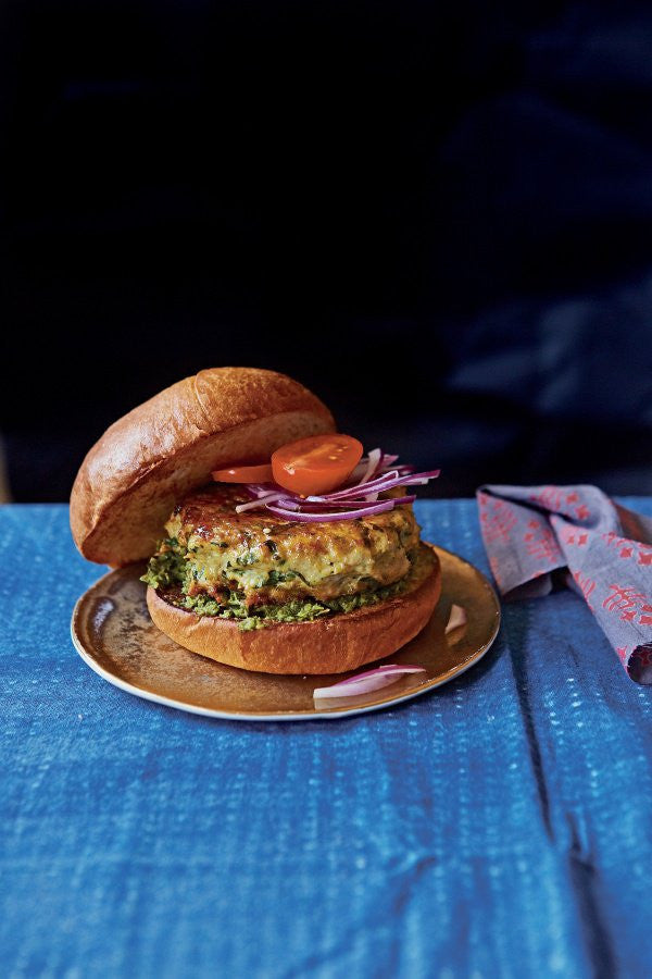 Mumbai-style chicken burger (or pattie) served in a toasted white bun, garnished with slices of red onion and fresh tomato