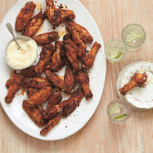 Platter of crispy baked chicken wings served with a pot of creamy garlic sauce and sparkling water with a slice of lime 