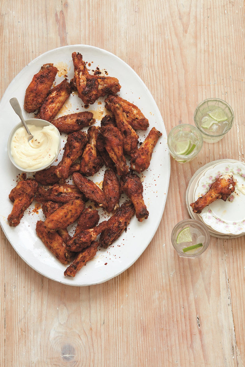 Platter of crispy baked chicken wings served with a pot of creamy garlic sauce and sparkling water with a slice of lime 