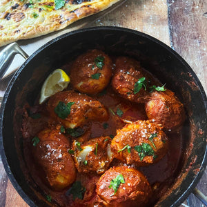 A pot full of Curry Guy’s Dum Aloo next to a Naan.