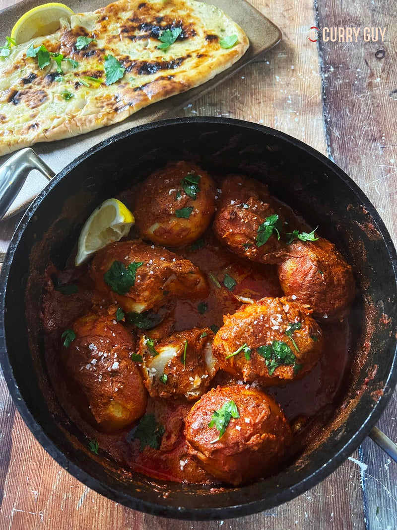 A pot full of Curry Guy’s Dum Aloo next to a Naan.
