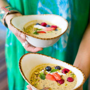 Hands holding 2 bowls of Saffron Chia Muesli garnished with fresh summer berries and mint leaves