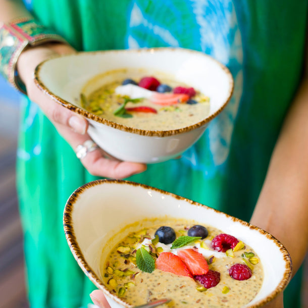 Hands holding 2 bowls of Saffron Chia Muesli garnished with fresh summer berries and mint leaves