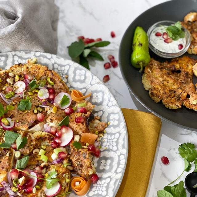 smoky shawarma-spiced cauliflower steaks, scattered with pomegranate seeds and spring onions, served with a raita dip