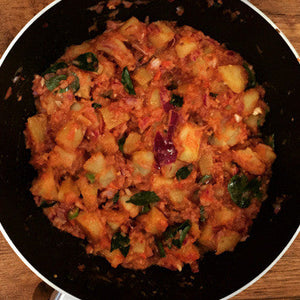 Spiced potato curry cooking in a pan with onions and herbs