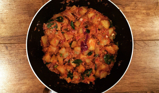 Spiced potato curry cooking in a pan with onions and herbs