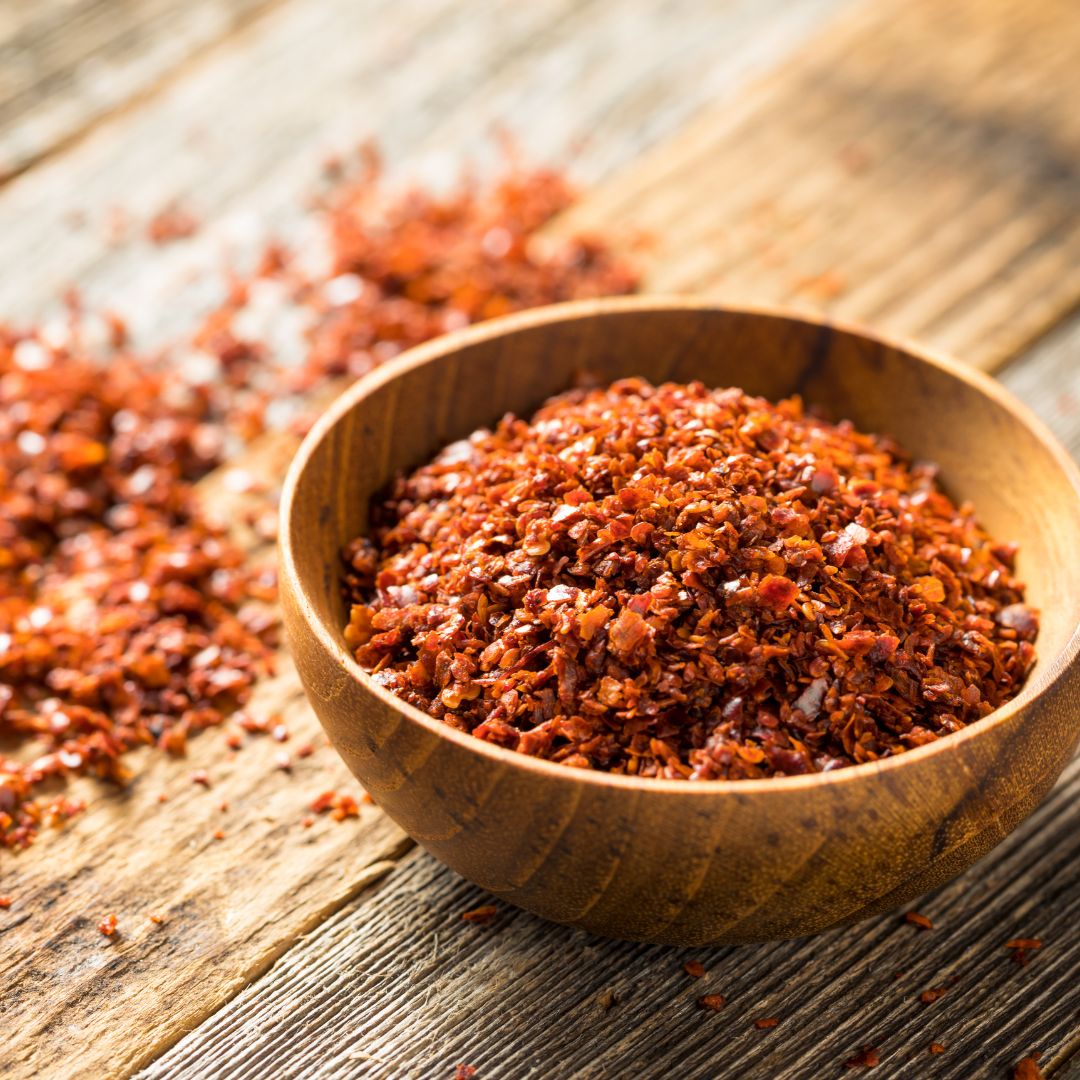 Wooden bowl filled with red Aleppo pepper flakes on a wooden surface