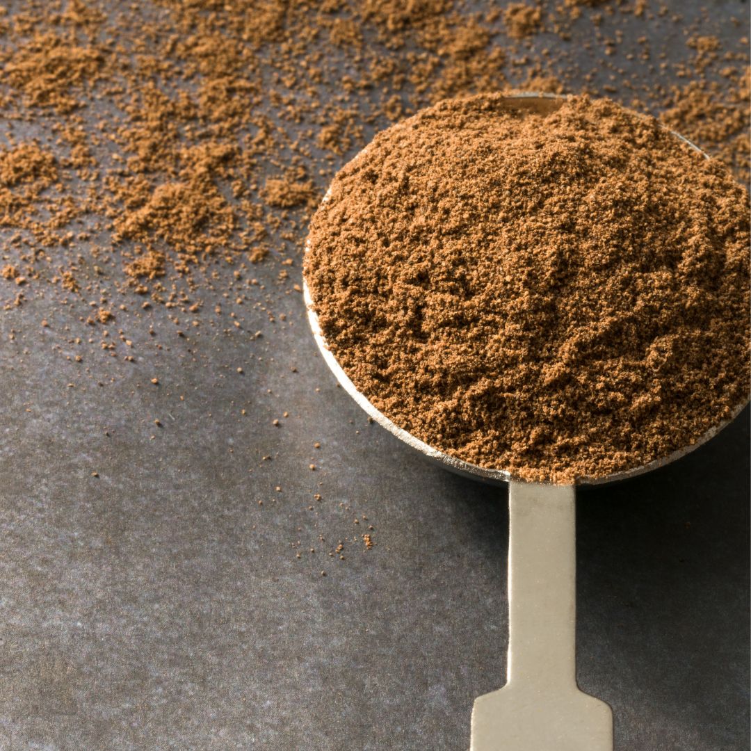 Spoon filled with ground allspice on a dark surface
