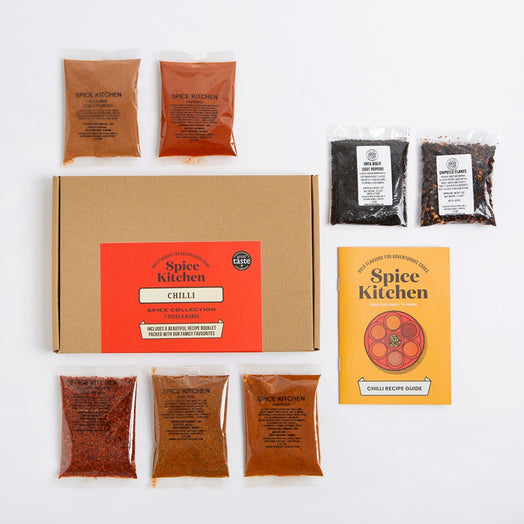 Spice Kitchen Chilli Spice Collection kit arranged on a white background, including a brown cardboard box with a red front label, seven small spice pouches and a yellow recipe guide booklet.