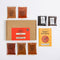 Spice Kitchen Chilli Spice Collection kit arranged on a white background, including a brown cardboard box with a red front label, seven small spice pouches and a yellow recipe guide booklet.