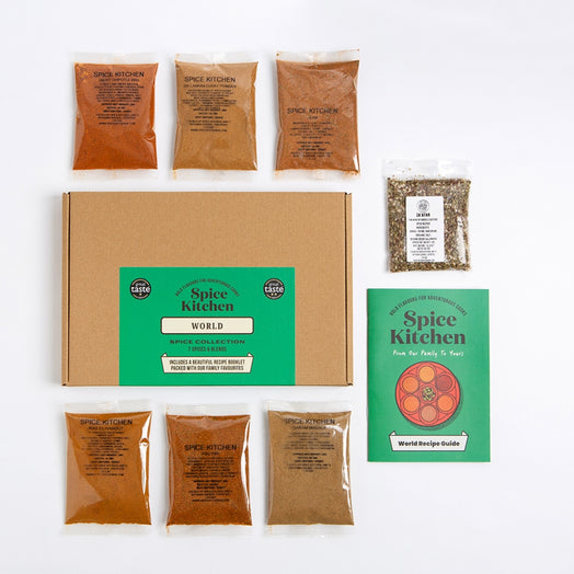 Spice Kitchen World spice collection set on a white background, featuring a brown cardboard box with a green label, seven small spice pouches and a green recipe guide booklet.
