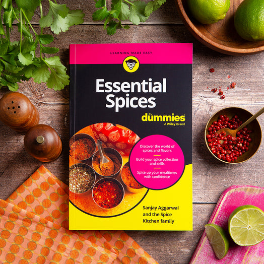 Sanjay Aggarwal's 'Essential Spices for Dummies' on a wooden surface with spices and herbs.