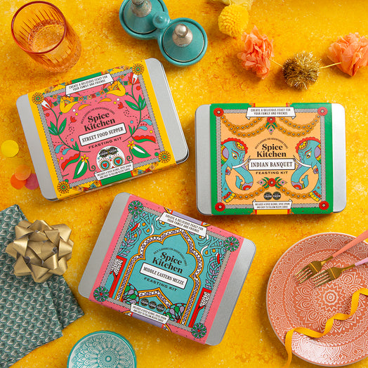 Three Spice Kitchen Feasting Kit tins on a yellow surface with decorative items.